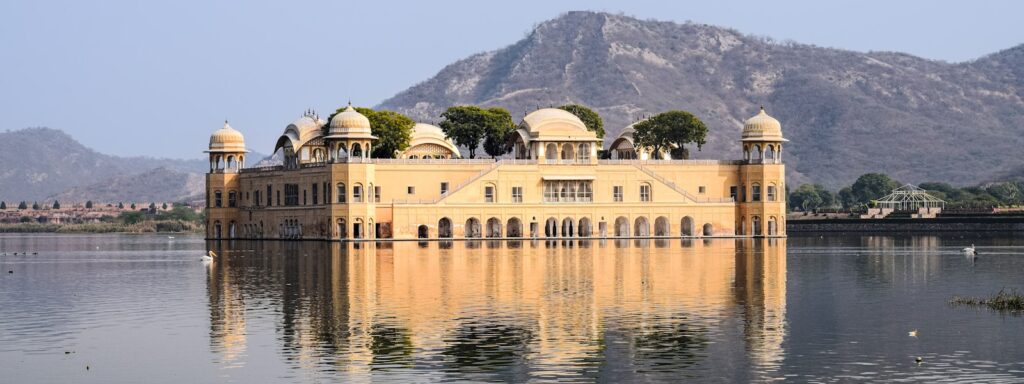 a large building with domed roofs by a body of water with Jal Mahal in the background